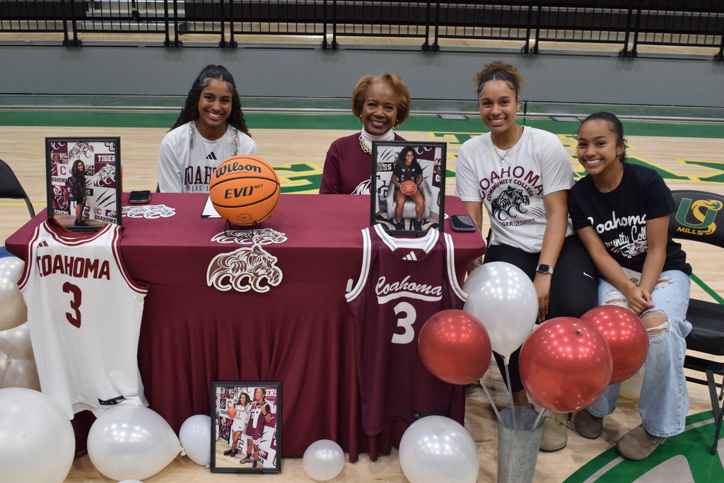 Four people sit behind a maroon table with Coahoma Community College logos, balloons, framed photos, and two Coahoma basketball jerseys. A basketball sits at the center.