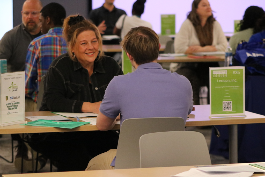 A representative from Lexicon, Inc. speaks with a student across a table. Signs list welding and ironworking careers. Other interview tables are visible in the background.