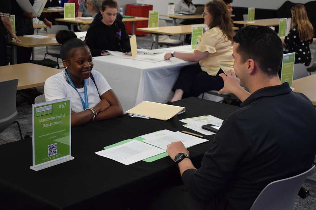 A representative from the Maumelle Police Department speaks with a student across a table. A green sign lists “Police Officer” as the available career.