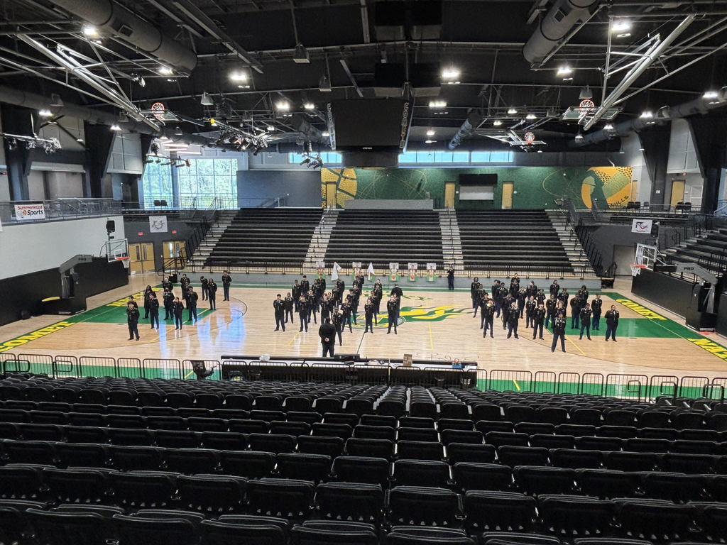 A wide view of dozens of Mills University Studies High School JROTC cadets standing in strict formation on the basketball court inside Cooper Arena during their JPA inspection.