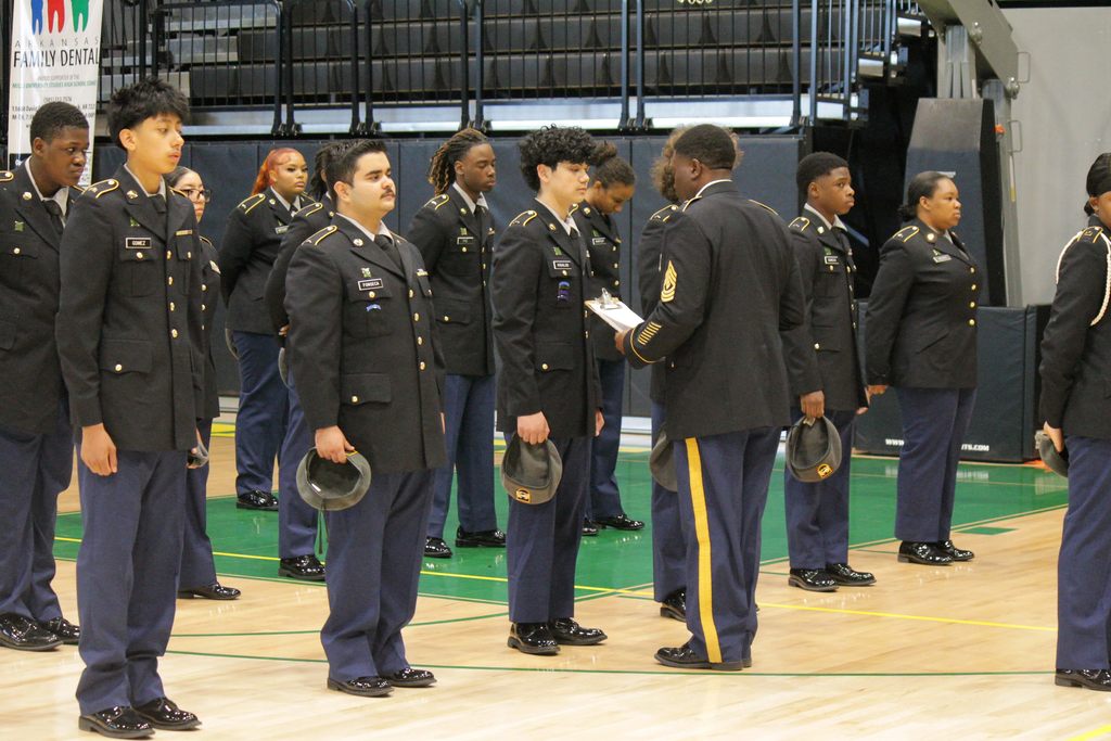 A U.S. Army JROTC instructor holding a clipboard while inspecting a line of Mills High School cadets, who are standing at attention in their dress uniforms.