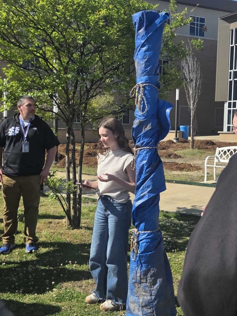 Students and adults gathered around the new Peace Pole in the Sylvan Hills High School courtyard, smiling and admiring the new installation.