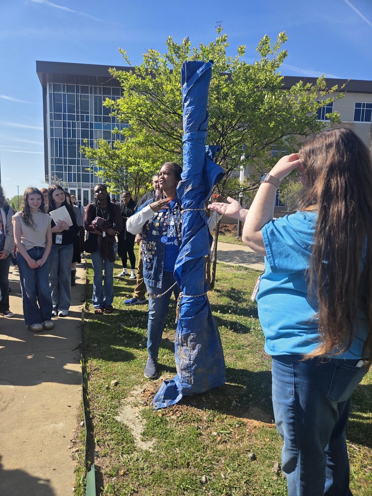 Students and adults gathered around the new Peace Pole in the Sylvan Hills High School courtyard, smiling and admiring the new installation.