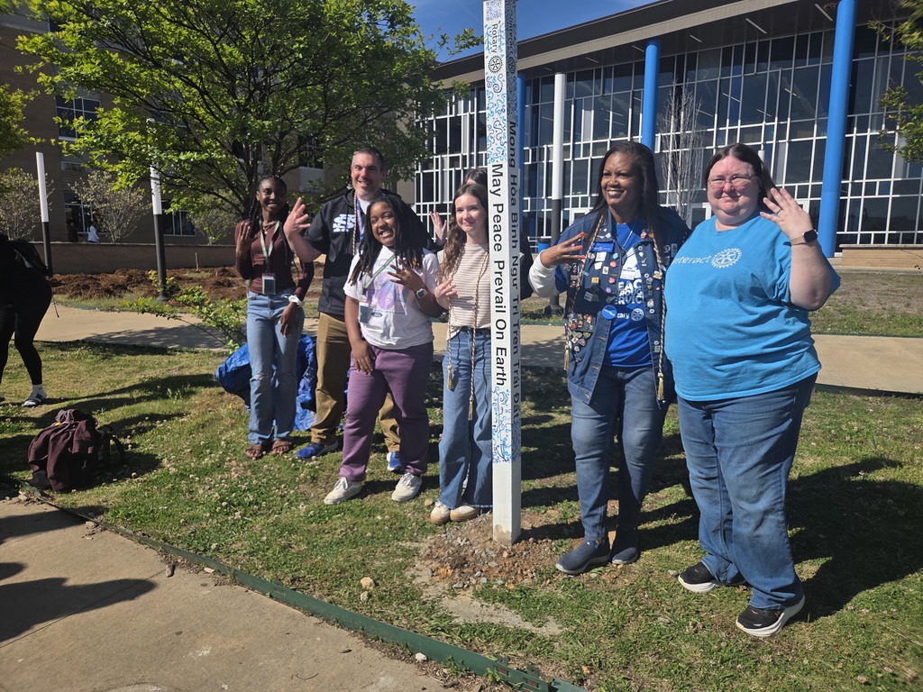 A large group of Sylvan Hills High School Interact students, school staff, and Sherwood Rotary Club members smiling together behind the newly installed white Peace Pole in the campus courtyard.