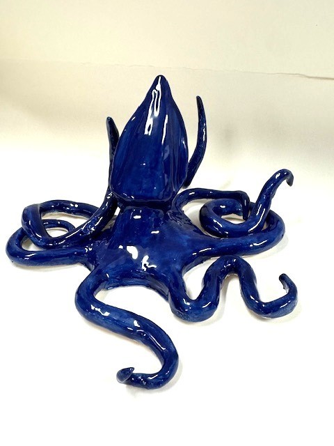 A glossy dark blue ceramic octopus with eight curled tentacles arranged around its body, displayed on a white background.