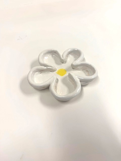 A small ceramic dish shaped like a five‑petaled flower, glazed white with a yellow circular center.