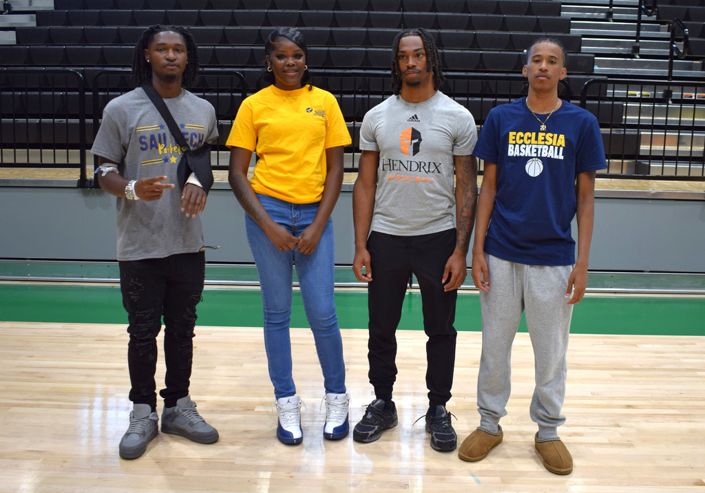 Four seniors stand on the gym floor wearing shirts representing SAU Tech, Hendrix, and Ecclesia. Bleachers are visible in the background.