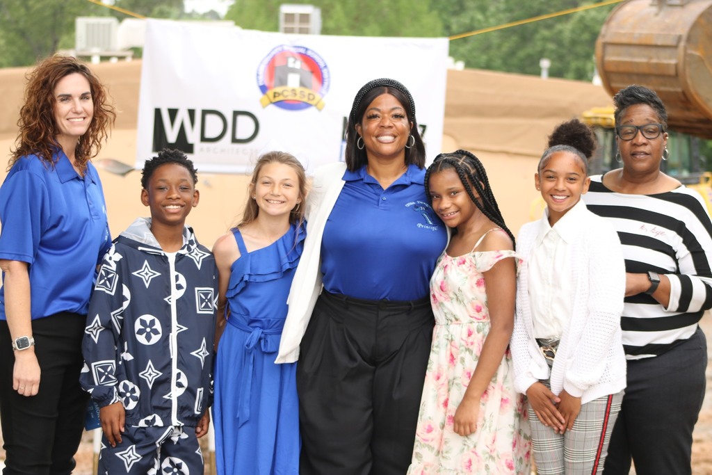 People smile in front of a sign for a construction project.