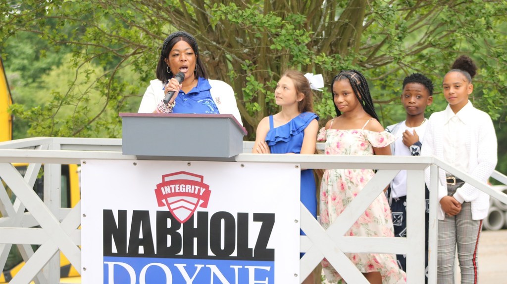Principal Angelica Evans speaking at the podium next to her students