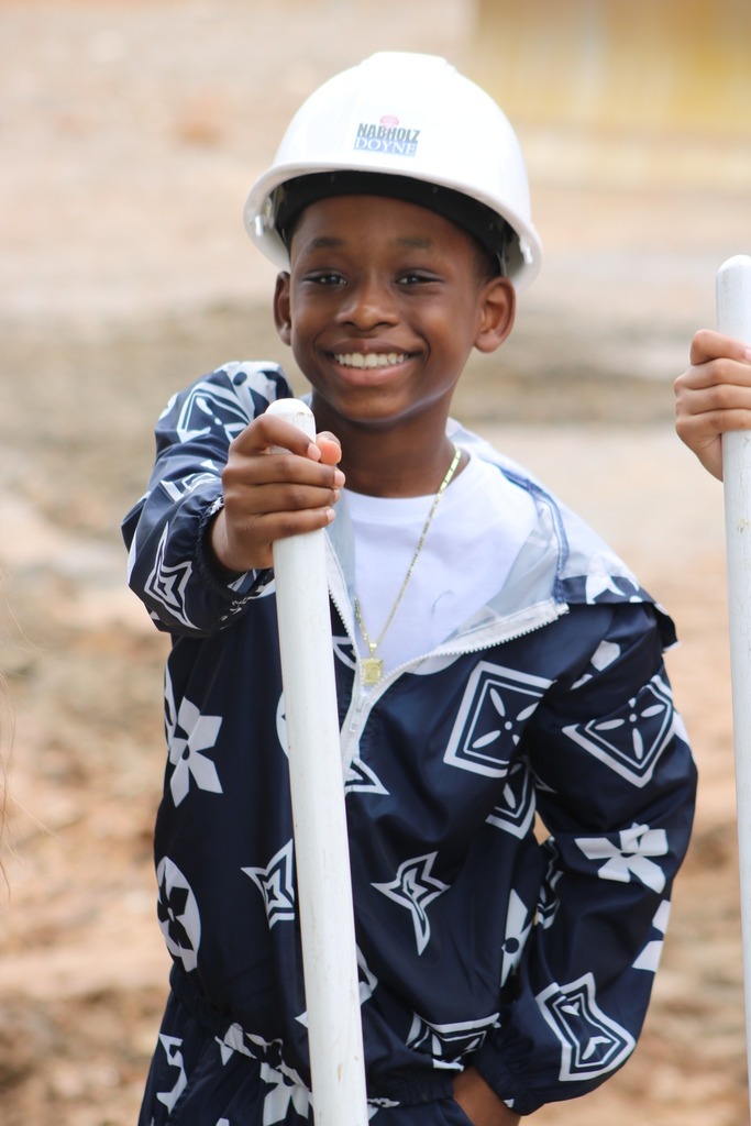 A boy in a hard hat holding a shovel.