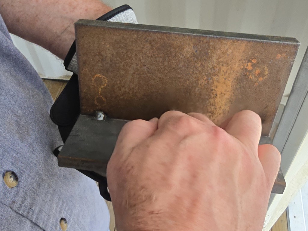 Close‑up of a rusted L‑shaped welded metal bracket resting on concrete next to a gravel area.