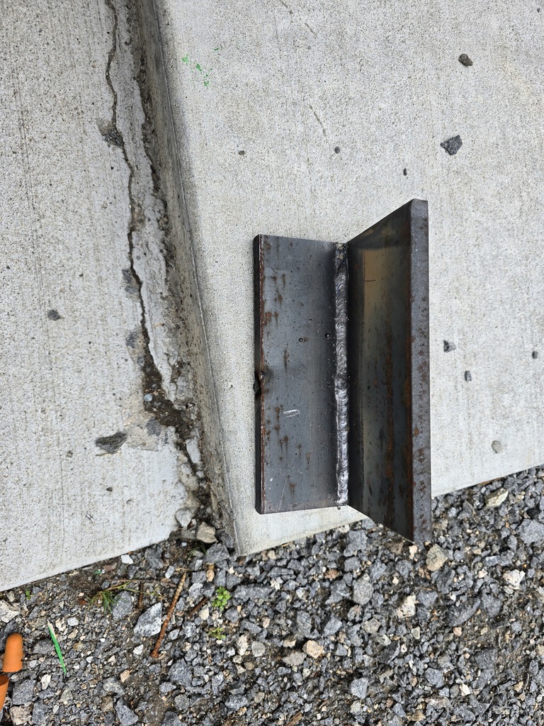 Close‑up of a student holding two steel plates welded together at a right angle. One hand is gloved and the other bare.