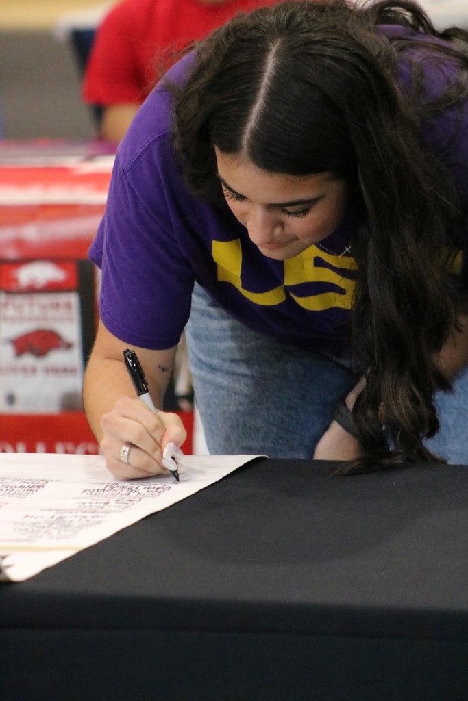 A student in a purple LSU shirt and jeans signs her name