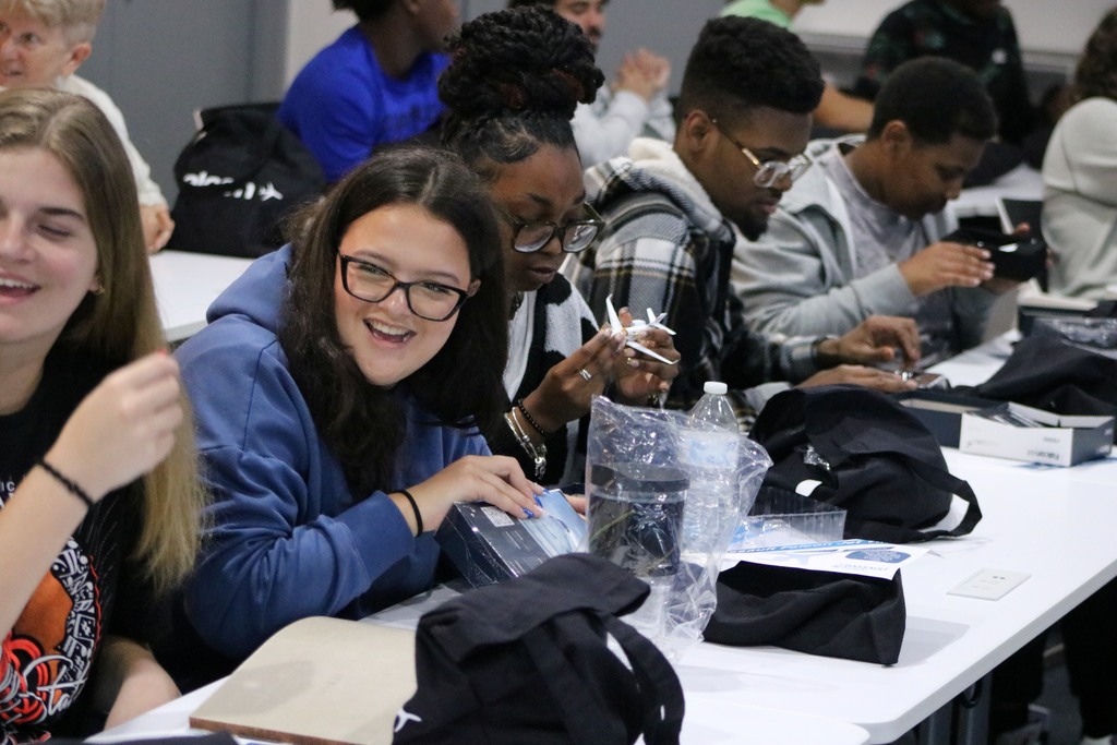 Students sit at tables examining small boxed items from a goody bag.