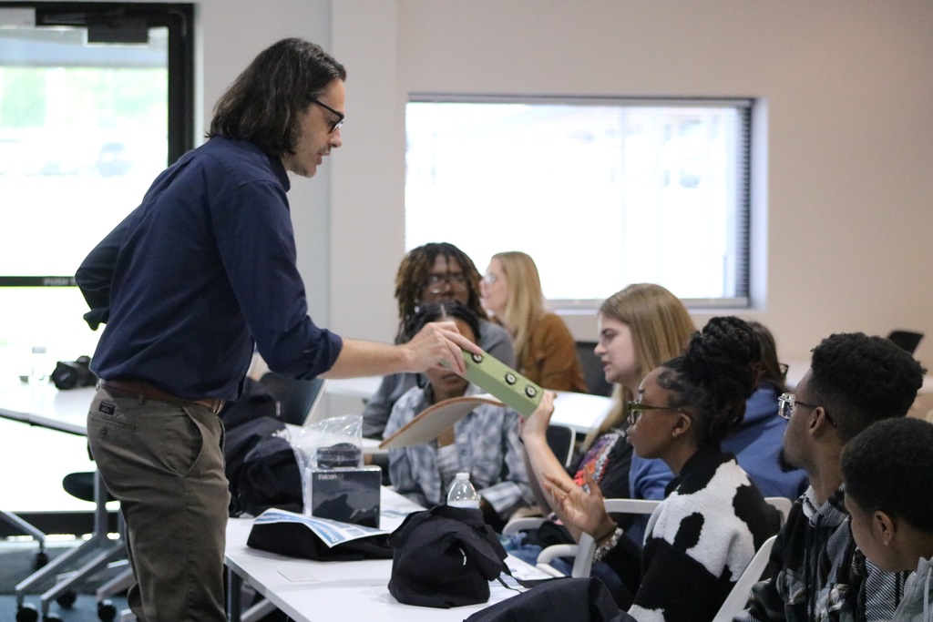 A staff member wearing a “Falcon” shirt passing around aircraft materials to students.