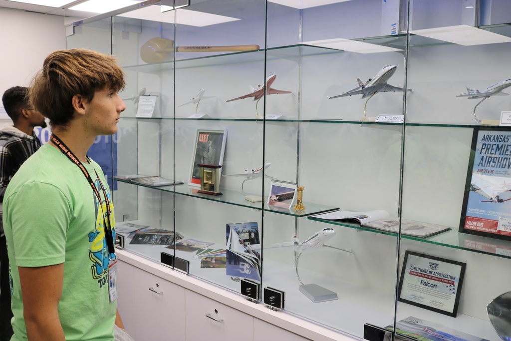 Two people stand in front of a glass display case filled with model airplanes, aviation memorabilia, framed documents, and a poster for an airshow.