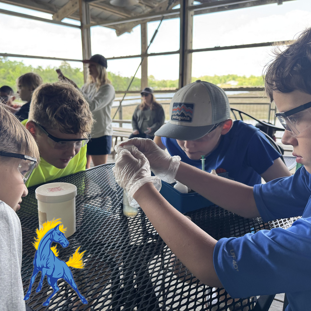 Students wearing goggles working with lab tools at a metal table during a science experiment.