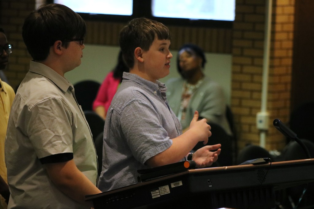 Two Sylvan Hills Middle School FBLA students stand at a podium speaking to the PCSSD school board. 