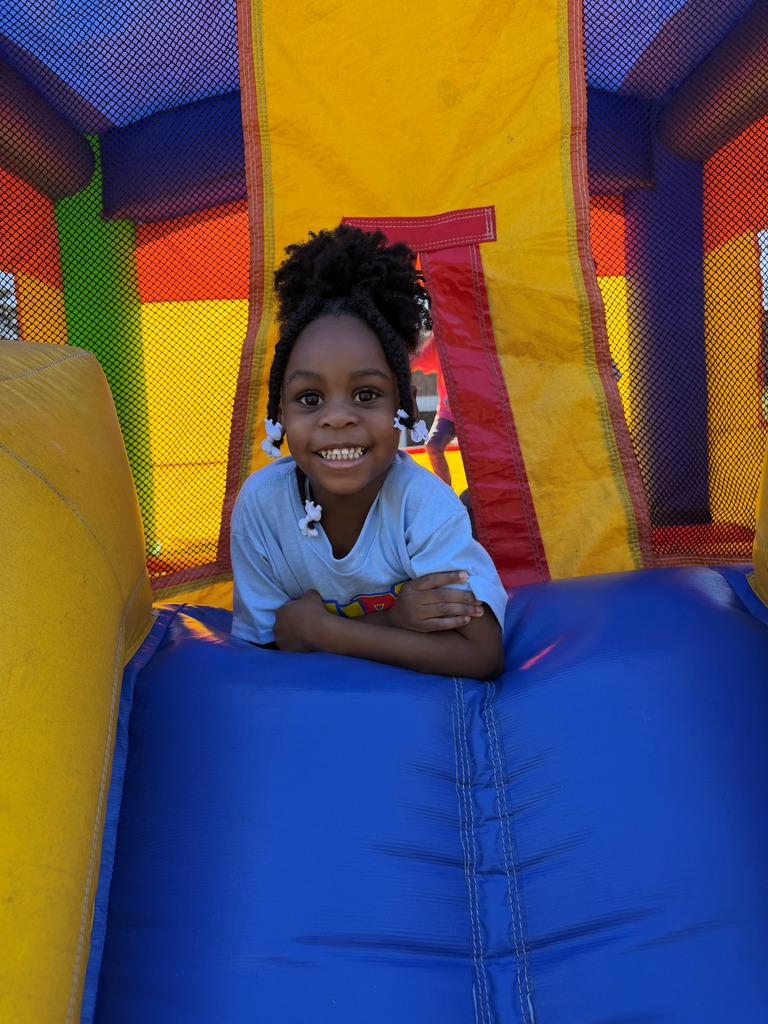 A child smiles while leaning on the blue edge of a brightly colored inflatable play structure.