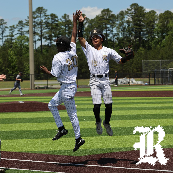 Two baseball players in white pinstriped uniforms jump and high‑five on the field.