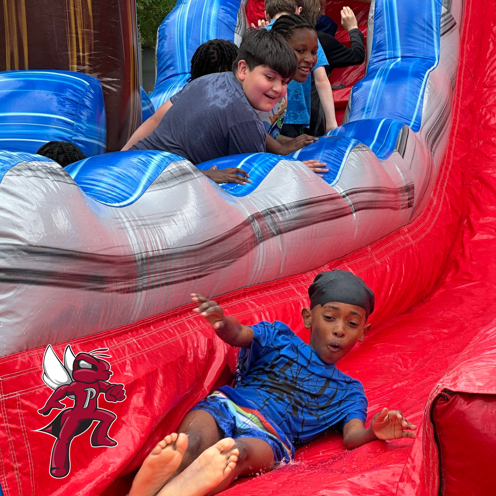Children play on a large inflatable water slide, with one child sliding down the front section.