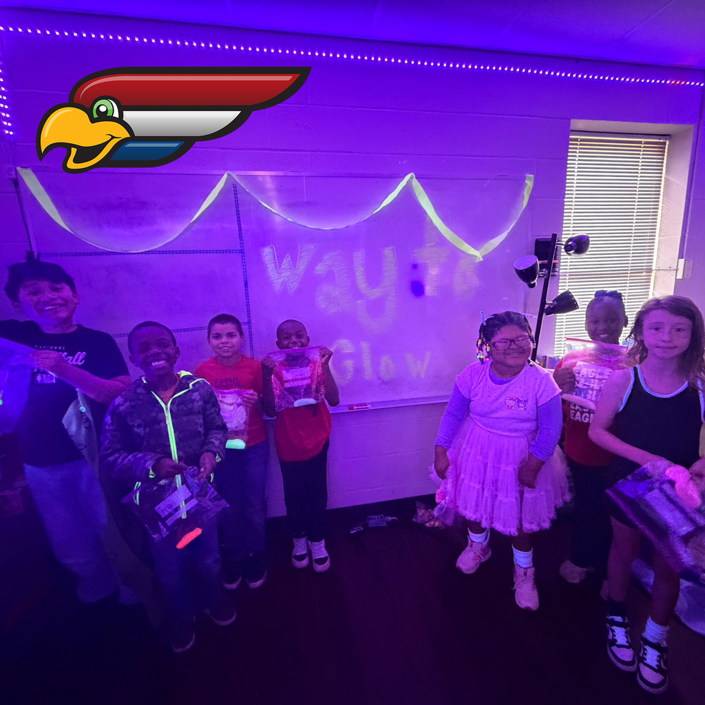 A group of children stand in a classroom lit with purple and blue glow lights, holding glowing objects beneath a “WAY TO GLOW” sign.