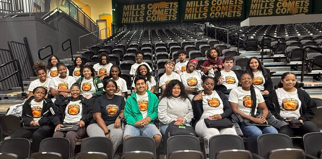 Large group of students sitting in an arena wearing matching tshirts