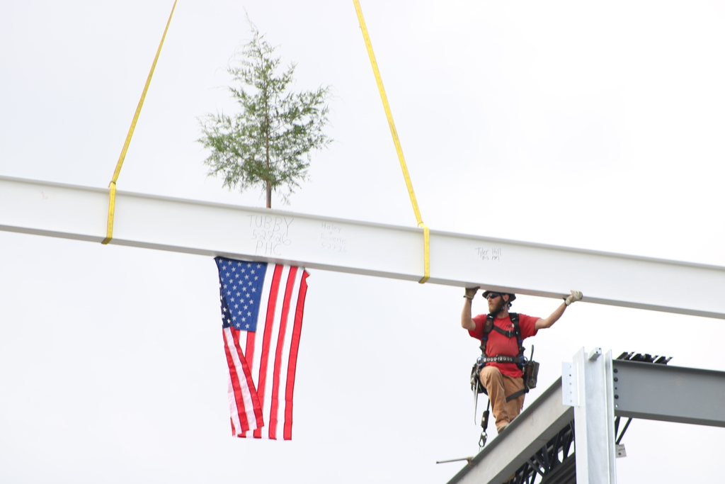 A construction worker steadies the ceremonial steel beam, decorated with an American flag and tree, during the topping out ceremony.