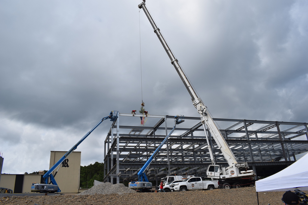 A crane lifts the ceremonial beam into place during the Joe T. Robinson High School addition topping out ceremony as workers guide the steel structure.