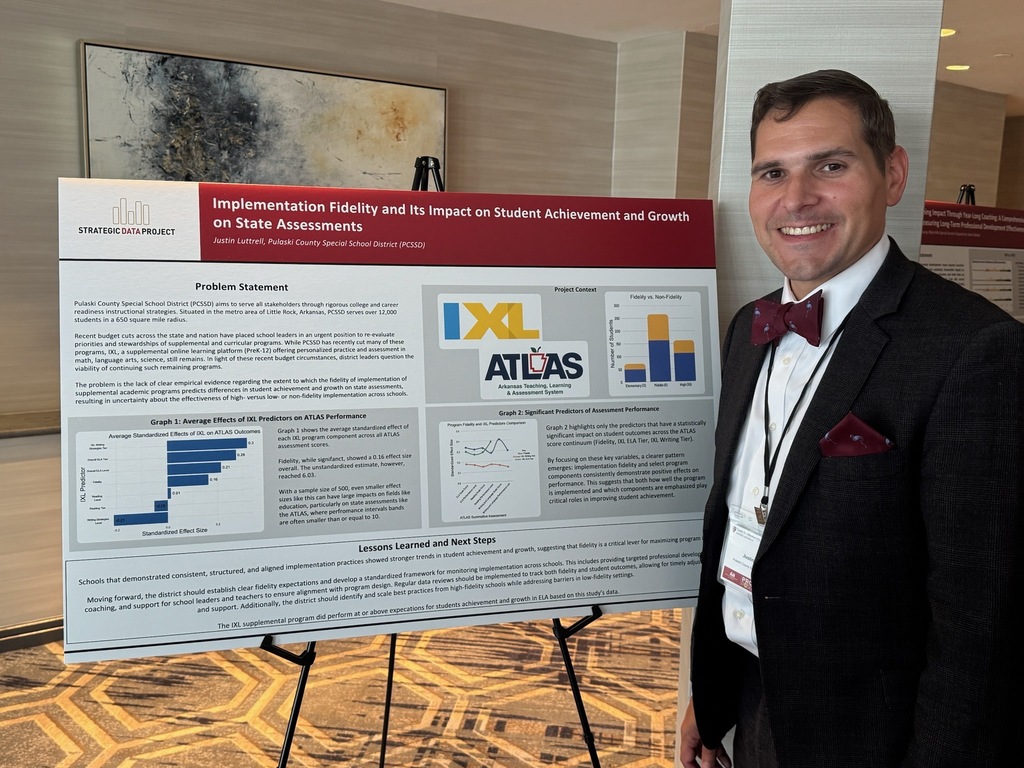 A person stands beside a research poster on an easel titled “Implementation Fidelity and Its Impact on Student Achievement and Growth on State Assessments.” The poster includes sections of text, bar charts, and logos for IXL and ATLAS. The setting appears to be a conference space with neutral walls and patterned carpet.