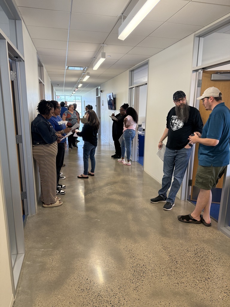 Staff members stand in a hallway discussing papers and materials during a break or transition in the AVID training day.