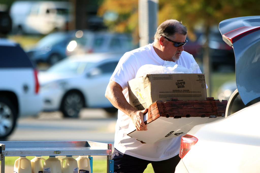 A man loads a box of food into a trunk. 