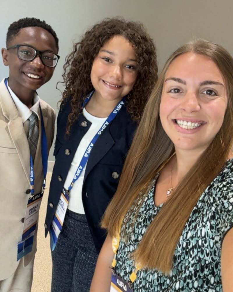 Two students and their teacher pose smiling for a picture