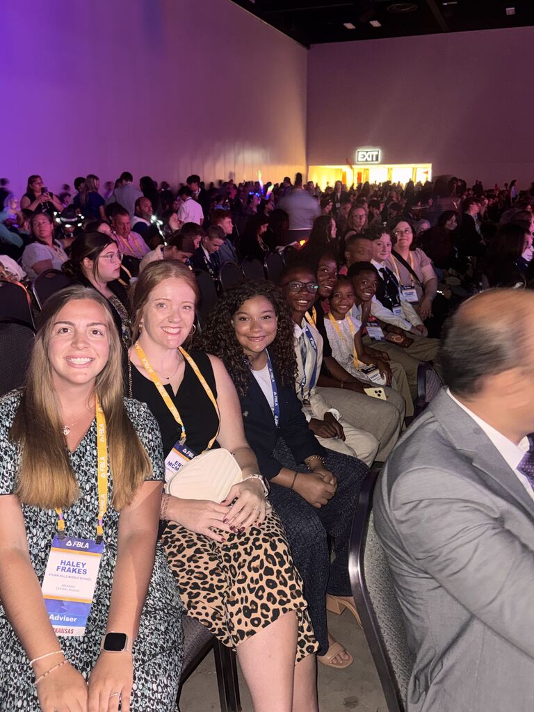 A picture of a packed auditorium. One row is smiling for a picture.