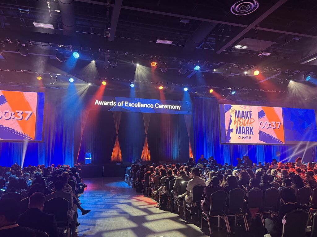A paked auditorim during a "Awards of Excellence Ceremony" a sign says "MAKE YOUR MARK FBLA" with a coundown time at 37 seconds.
