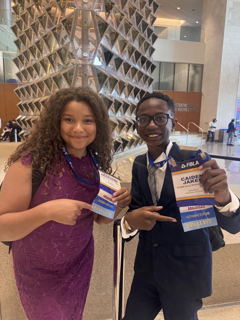 Two students hold their FBLA lanyards smiling and point to their finalist ribbon.