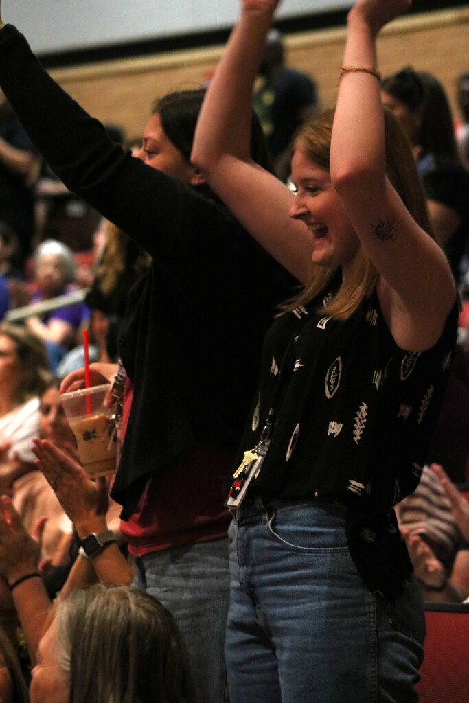  Two people stand with arms raised in celebration inside an auditorium filled with seated staff.