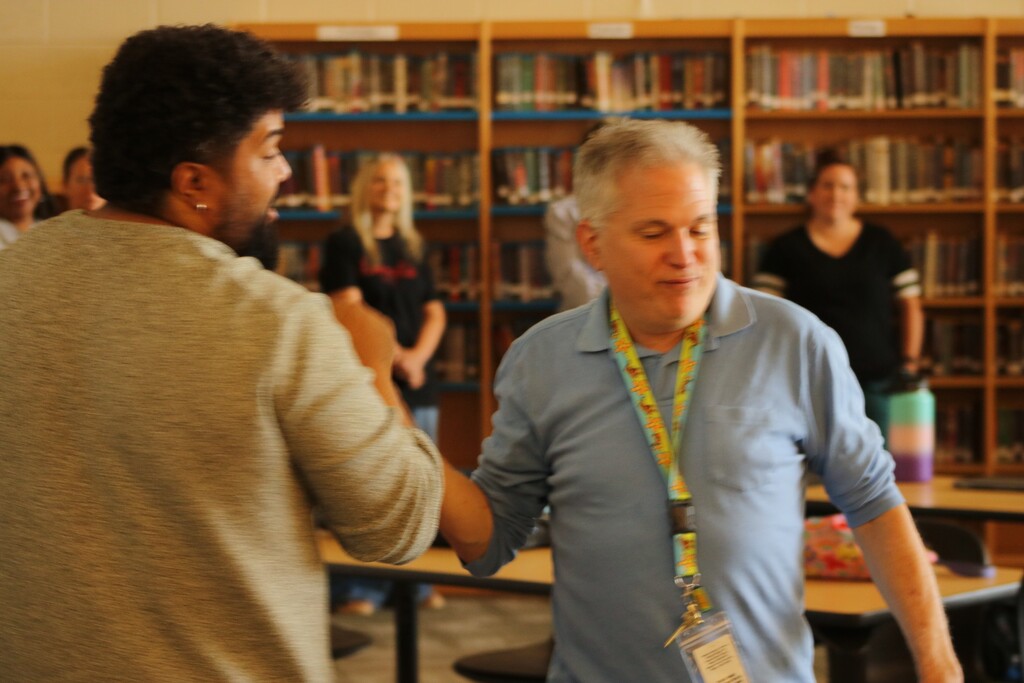 Staff at Maumelle High School stand in a circle during a professional‑development activity, taking turns introducing themselves and sharing something they enjoy.