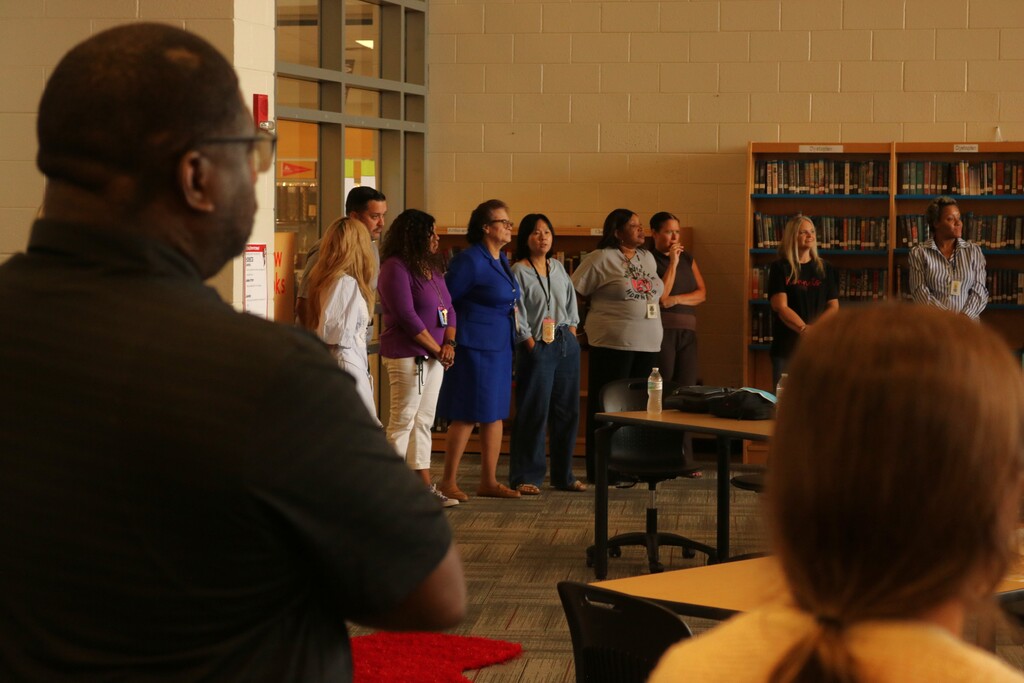 Staff at Maumelle High School stand in a circle during a professional‑development activity, taking turns introducing themselves and sharing something they enjoy.