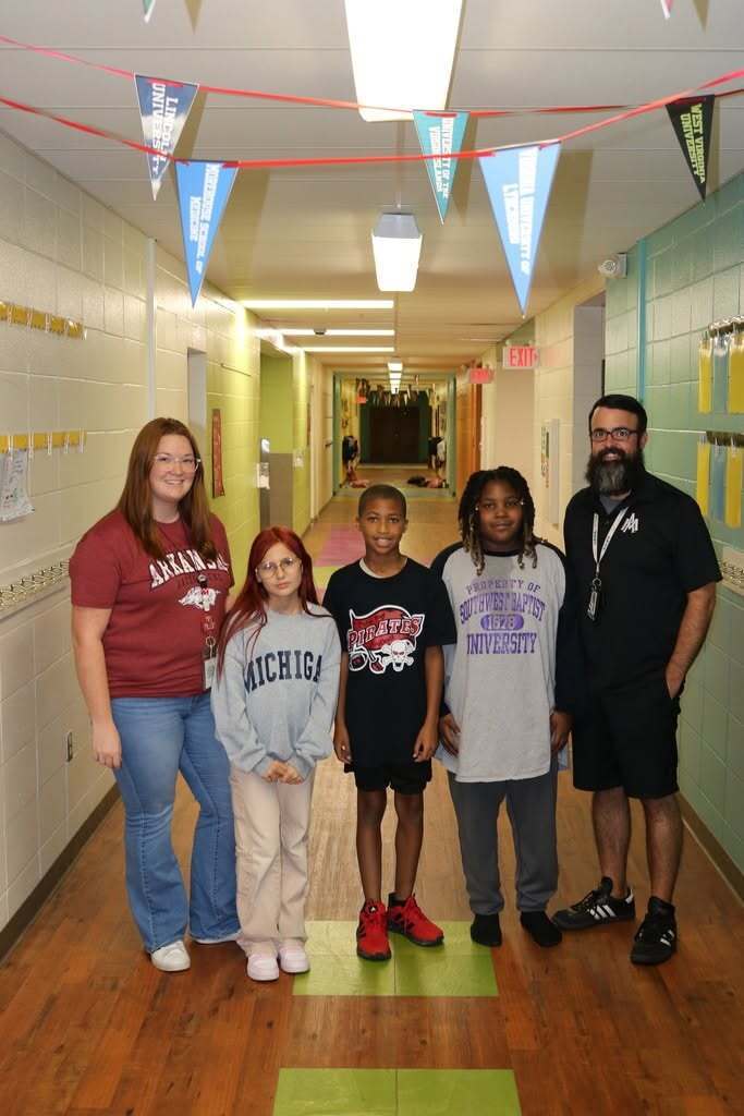 Teachers and students in a hallway smiling with college shirts on
