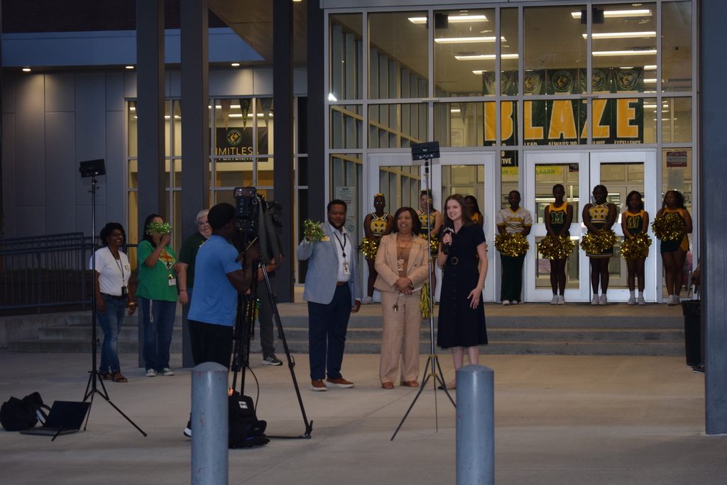 A group of people standing in front of a building with large "BLAZE" text on the façade. There are cameras and equipment, indicating a media or filming event.