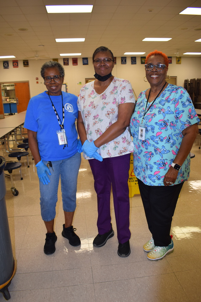 Three female staff members posing for a photo in a hospital setting, wearing colorful uniforms and scrubs.