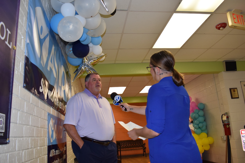 A man in a white shirt and a woman in a blue shirt standing and interacting in a room decorated with balloons.