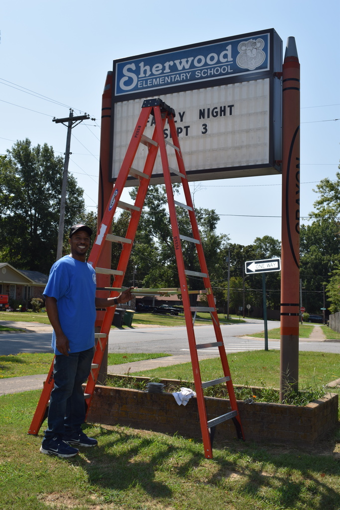 Sherwood Elementary School sign with red ladder against a blue sky and trees in the background.