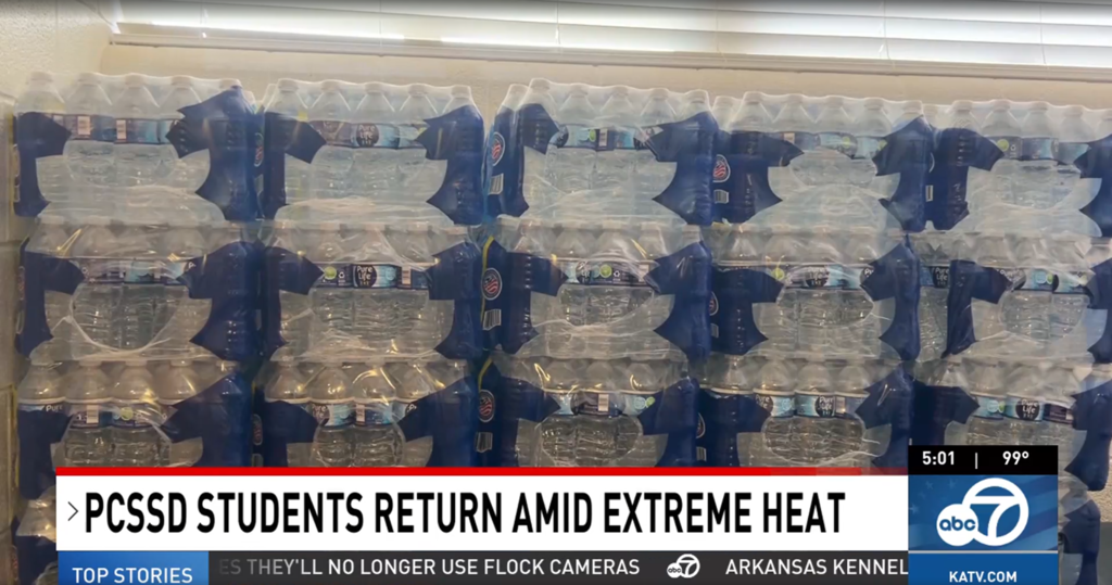 Rows of water bottles with "PCSSD STUDENTS RETURN AMID EXTREME HEAT" displayed below them.