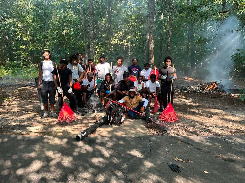 A group of men with yard cleaning equipment posing for a picture in a park