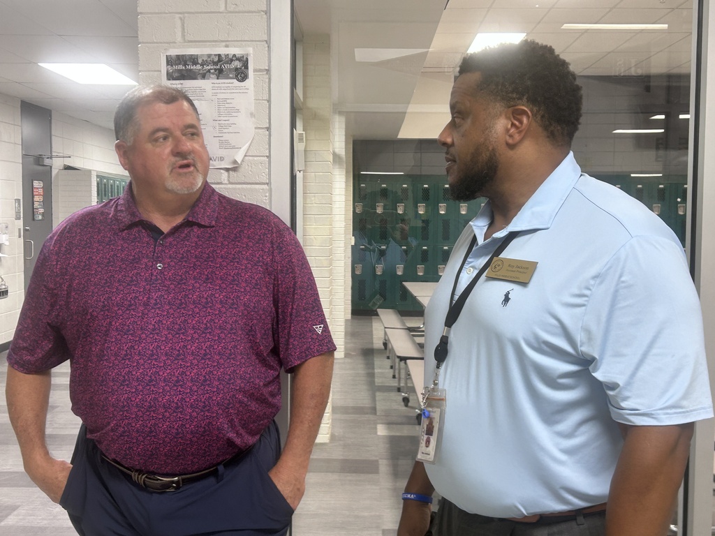 Two men in casual work attire having a conversation in a school hallway.