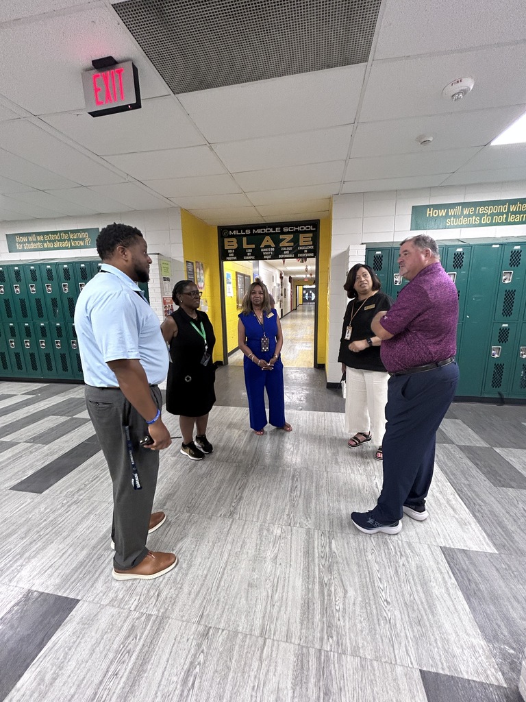 Group of educators standing in school hallway with lockers and school signage.