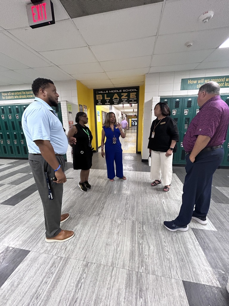 Group of educators standing in school hallway with lockers and school signage.