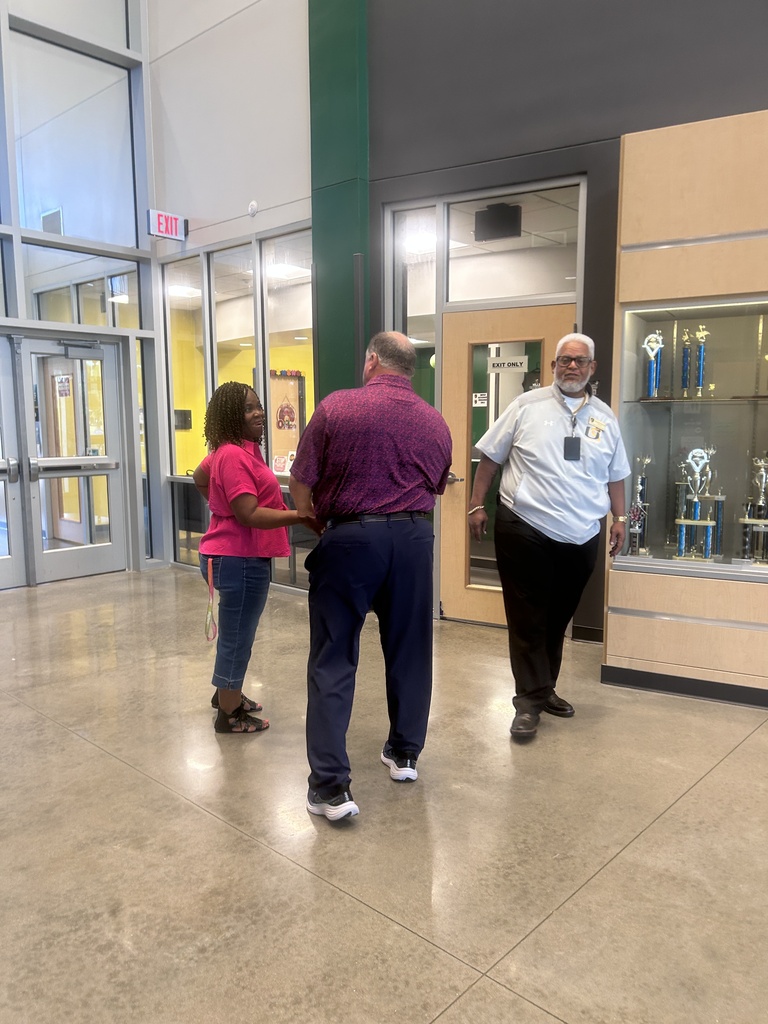 Three people standing in a lobby, one in a purple shirt, one in a red shirt, and one wearing a white uniform.